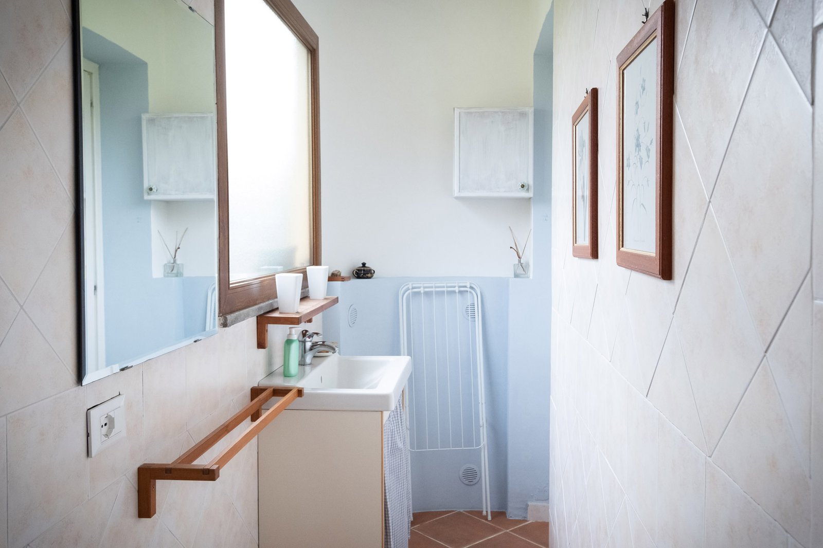 bagno con lavello moderno bianco di fronte a una grande finestra lumionsa e sullo sfondo uno  stendino per i panni e un armadietto