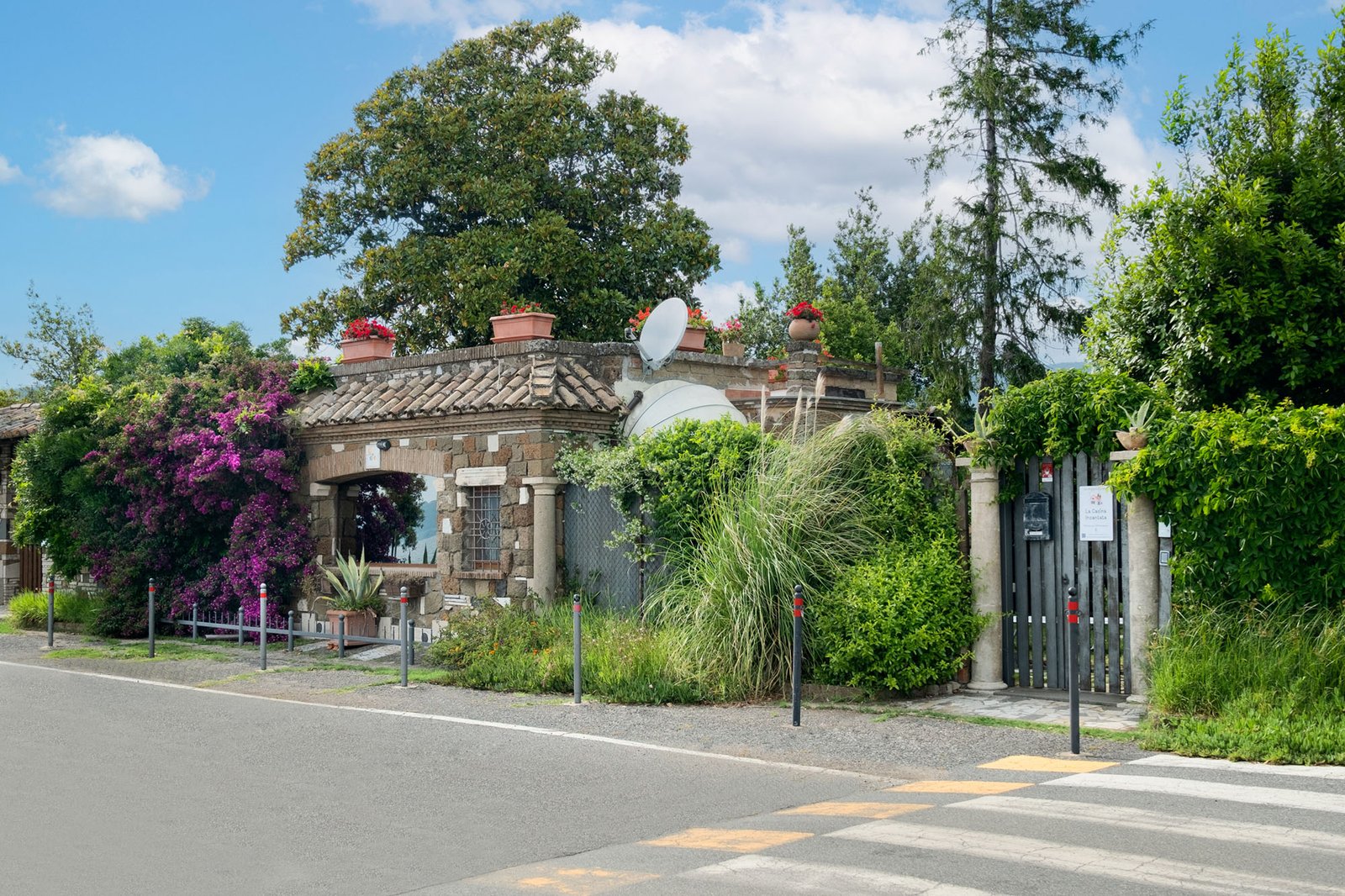 casa a mattoncini con grandi vetrate e molte piante intorno con accesso del giardino su strada